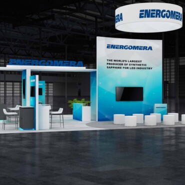 Front view of an Energomera booth with a circular hanging sign, turquoise displays and white seating.