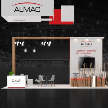 Almac booth with suspended branding, a wood-effect display wall and a small meeting area.